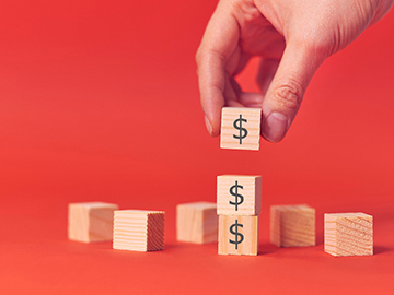 Hand stacking wooden blocks marked with dollar signs